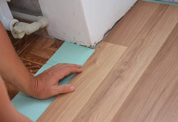 Muž instalaci laminátových parket v problémové oblasti. Pracovní instalace dřevěné plovoucí podlahy. Údržbář, kterým se stanoví laminátové podlahy prkna při rekonstrukci domu. — Stock fotografie