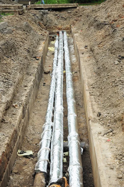 Tubos de água em uma trincheira de barro. Reparação e substituição de esgoto com isolamento para economia de energia . — Fotografia de Stock