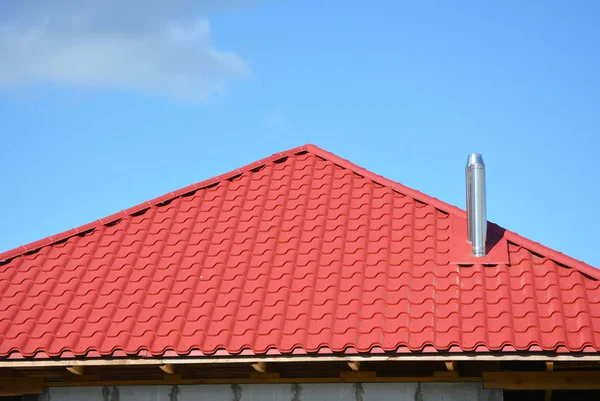 Red metal roofing construction. Metal modular coaxial chimney with red metal sheets house roof. Roofing Construction.