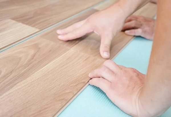 Contractor installing wooden laminate flooring with insulation and soundproofing sheets. Man laying laminate flooring. Man laying laminate flooring.