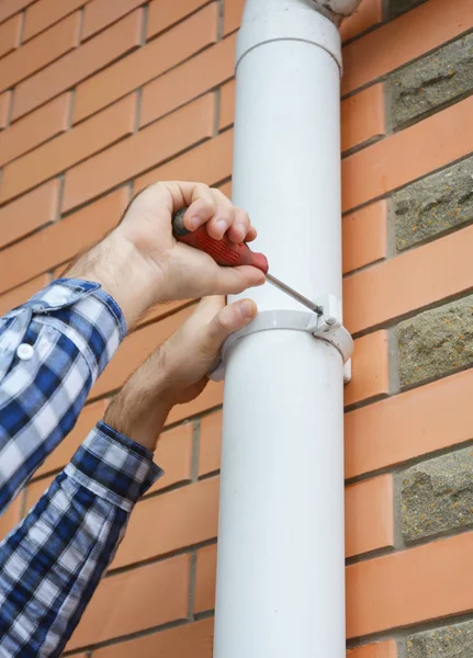 Worker Installing rain gutter downspout pipe. Contractor hands repair rain gutter downspout pipe with screwdriver. Guttering, Rain Chain, Plastic Guttering & Drainage. Guttering Down pipe Fittings