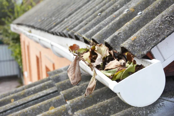 Roof gutter with fallen leaves in autumn. Rain gutter cleaning. — Stock Photo, Image