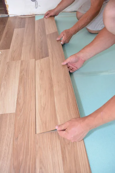 Contractors installing wooden laminate flooring with insulation and soundproofing sheets. Man laying laminate flooring.