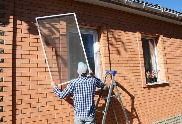 Trabajador instalar mosquitero o mosquitero pantalla de alambre en ventana de la casa de ladrillo . — Foto de Stock