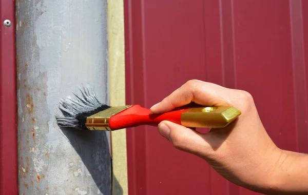 Painting metal fence with worker hand. Painting fence with red brush.