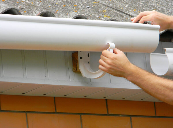 Contractor installing plastic roof gutter. Plastic Guttering, Rain Guttering & Drainage by Handyman hands. 