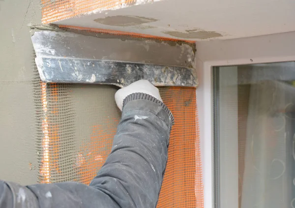 Pared de enlucido del contratista con cuchillo de masilla, malla de fibra de vidrio, malla de yeso después del aislamiento rígido. Casa pared problema área aislante con estuco pared . — Foto de Stock