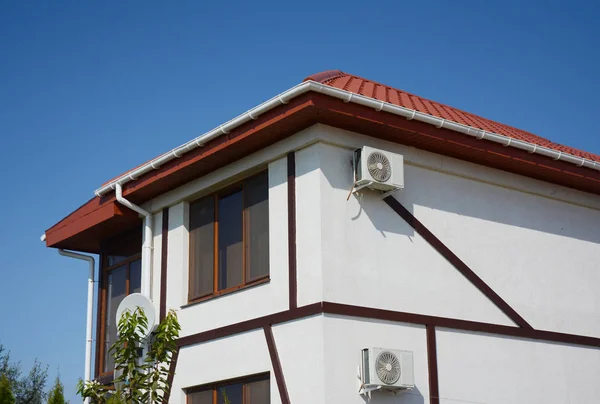 Weißes Fassadenhaus mit Ziegeldach, Kunststoffdachrinne und Luftkompressoren. — Stockfoto