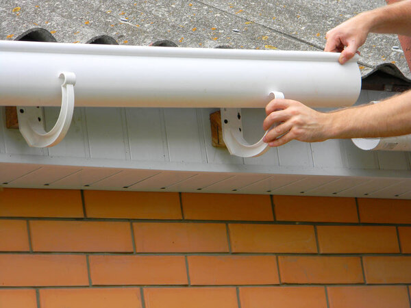 Contractor installing plastic roof gutter. Plastic Guttering  Replace, Rain Guttering & Drainage Repair by Handyman hands. 