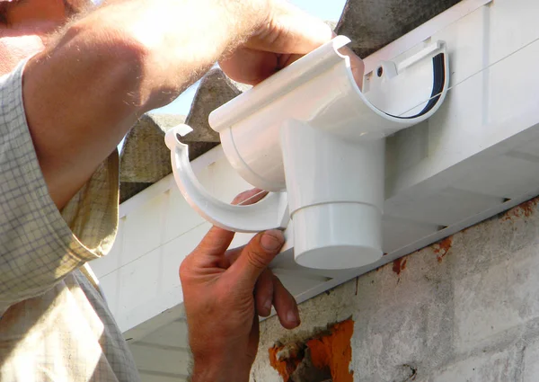 Entreprenören installera plast tak rännan hållare för dowspout avloppsrör. Plast takrännor, regn rännor — Stockfoto
