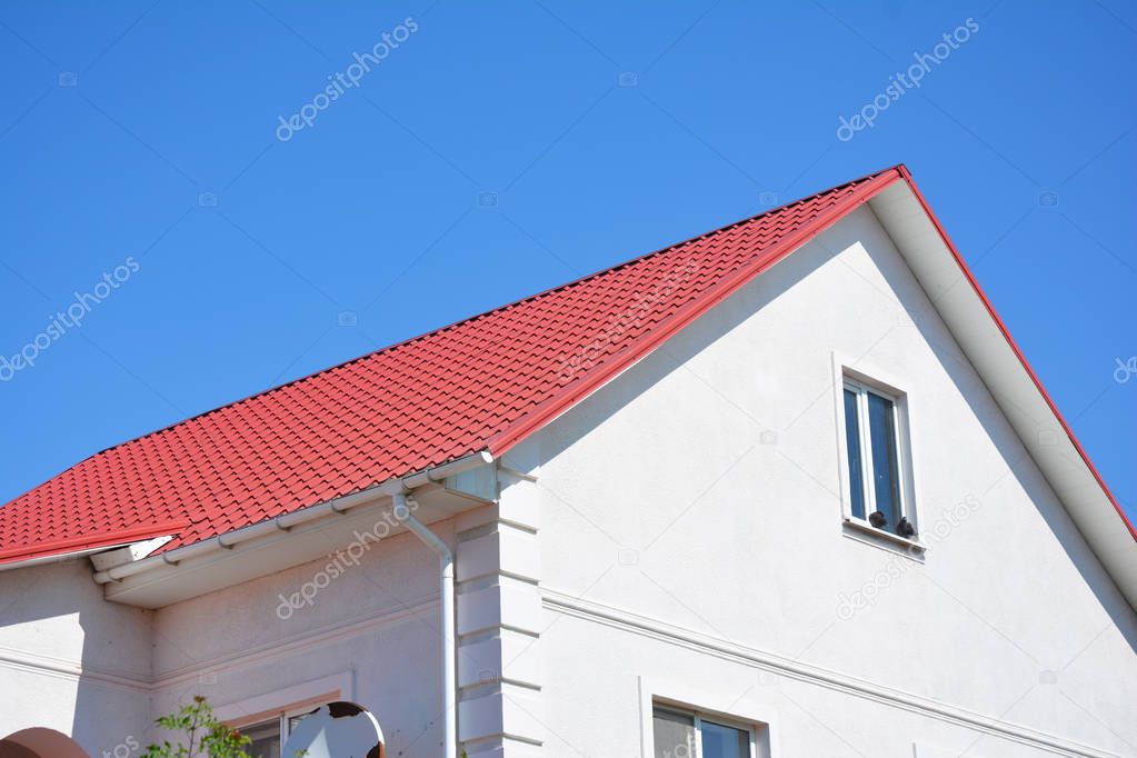 House with plaster walls, attic window,  red metal roof and white plastic rain gutter. Roofing construction.