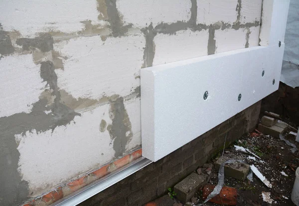 External house wall insulation with styrofoam. Installing rigid foam insulation board on house wall outdoors. Attach rigid foam insulation to a house wall
