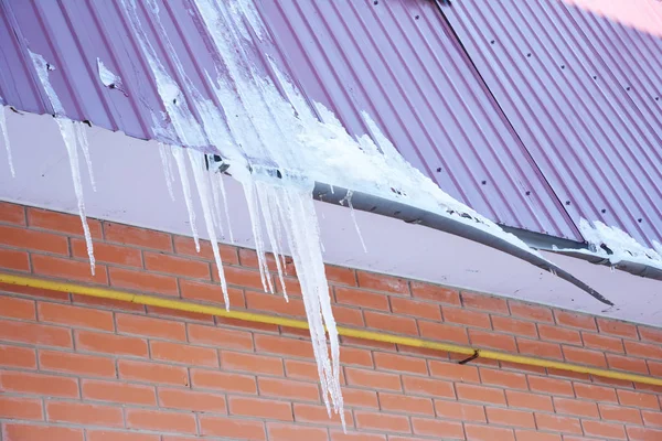 Roof Gutter damaged by ice and snow. Broken house roof gutter pipeline by icicles.