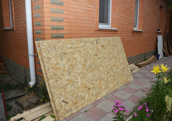 Tablero de filamento orientado (OSB) cerca de la pared de la casa de ladrillo —  Fotos de Stock