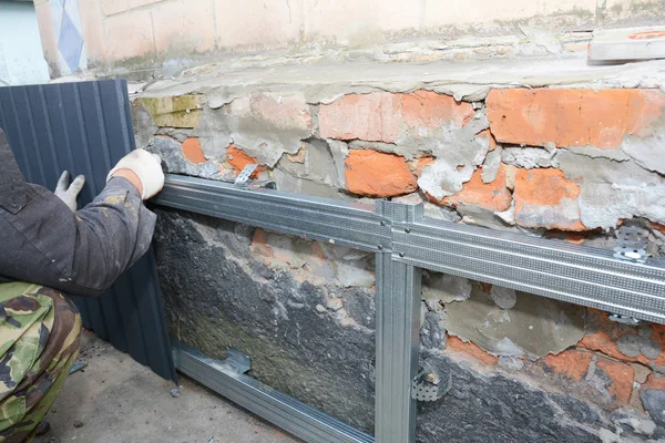 レンガハウスの基礎壁の修復、防水と雨から保護するための金属シートをインストールするビルダーの手で改装. — ストック写真