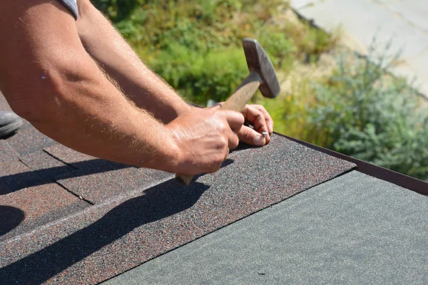 Takläggare händer installera asfalt bältros på hus konstruktion tak hörn med hammare och spikar i rörelse. Takläggning Konstruktion Foto. — Stockfoto
