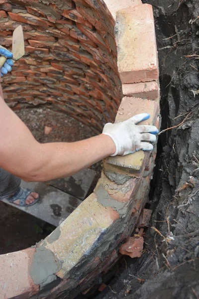 Builder installing septic tank wall from brick  on house construction site
