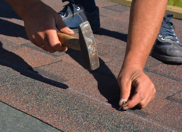 Dachowy wykonawca układa gonty asfaltowe. Budowa dachu domu z gontem dachowym. Roofer młotkowanie gwóźdź w asfalcie gonty na dachu domu. — Zdjęcie stockowe