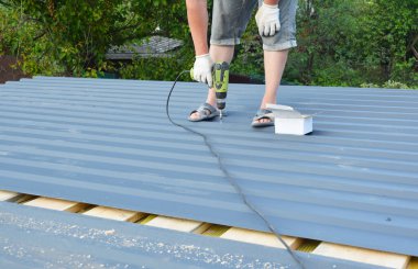 Corotile hafif metal çatı levhaları monte eden vida tabancalı bir çatı tamircisi.