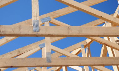 Çatı iskeleti sahnesinde tamamlanmamış çatı inşaatı kirişleri, kirişler mavi gökyüzüne karşı yapılır..