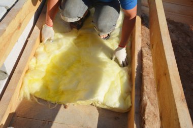 Bir inşaat müteahhidi çatı kirişleri arasında kılıfın altına mineral yün termal yalıtım uyguluyor..