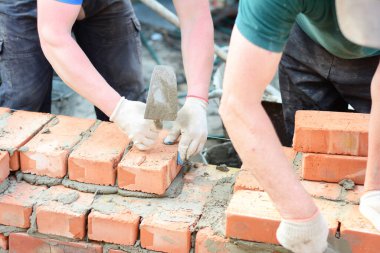 Masons in protection gloves are laying bricks applying mortar, concrete using a trowel to build a brick wall of a house construction. clipart