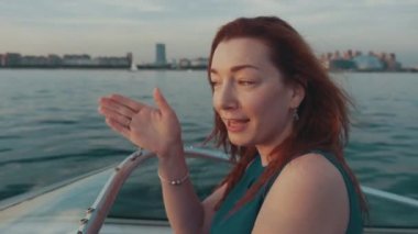 Kızıl saçlı kız turkuaz elbiseyi sürücü Motorlu tekne çocukla konuş. Yaz gecesi.