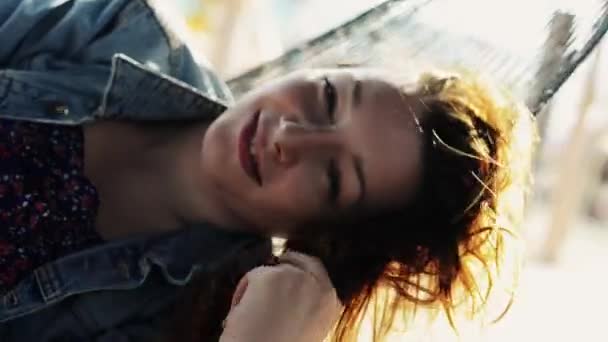 Chica joven y feliz balanceo en hamaca en la playa sonrisa en la cámara. Día soleado. Agitar el cabello — Vídeos de Stock