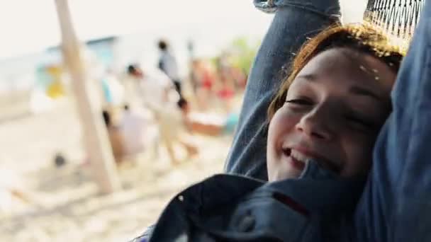 Glückliches junges Mädchen wiegt sich in der Hängematte am Strand und lächelt in die Kamera. Sommer sonniger Tag. — Stockvideo