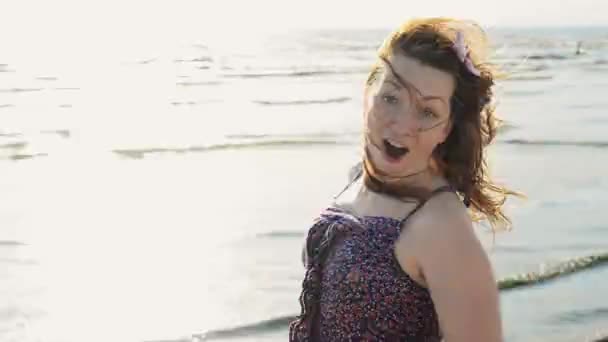 Chica joven feliz con flor en el pelo rápidamente ejecutar en la playa sonrisa en la cámara. Soleado. . — Vídeo de stock