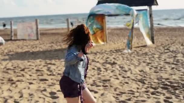 Glad ung flicka kör på stranden. Le i kameran. Ta bort jackan. Sommardag. — Stockvideo