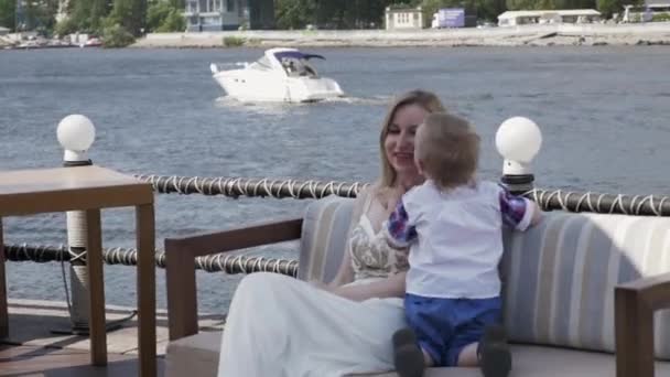 Mère posant avec son petit fils sur le canapé en bord de mer. Événement. Terrasse du restaurant . — Video