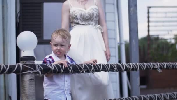 Mor i aftonklänning med lille son på terrassen vid floden. Händelse. Sommardag — Stockvideo