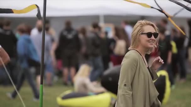 Petrohrad, Rusko - 16 července, 2015: Blondýnka ve sluneční brýle pózuje na kameru mezi černá a žlutá mává pásky. Letní festival — Stock video