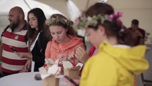 Sankt Petersburg, Ryssland-16 juli 2015: unga flickor med blomma krans på huvudet med lunch från lådor på Summer Festival. Underhållning. — Stockvideo