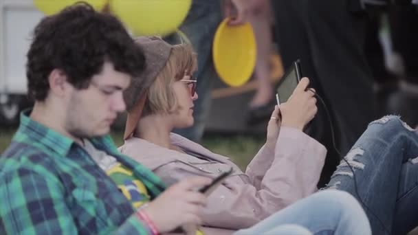 SAN PETERSBURG, RUSIA - 16 DE JULIO DE 2015: Jovencita con gorra, el hombre juega en las tabletas en el festival de verano. Día soleado. Evento de entretenimiento. Día soleado — Vídeo de stock