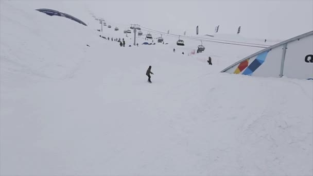 СОЧИ, РОССИЯ - 29 МАРТА 2016 года: Сноубордист скользит по железной изогнутой тропе, делает флип на горнолыжном курорте в горах. Крайне. Снег падает — стоковое видео