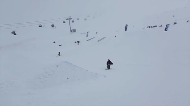 SOCHI, RUSIA - 29 DE MARZO DE 2016: Salto snowboarder desde trampolín en pendiente, flexiona los pies. Estación de esquí en montañas nevadas. Desafío . — Vídeos de Stock