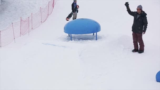 SOCHI, RUSIA - 29 DE MARZO DE 2016: Salto snowboarder en pateador pospuesto fuera de borda en la estación de esquí. Montañas nevadas. Deporte extremo. Camarógrafo . — Vídeos de Stock