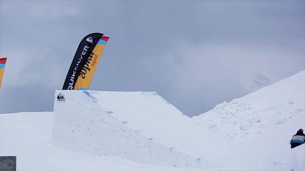 Sochi, Oroszország-március 29, 2016: Snowboarder egységes ugrás ugródeszka. Hegyek. Táj. Extrém sportok. Szürke égbolt — Stock videók