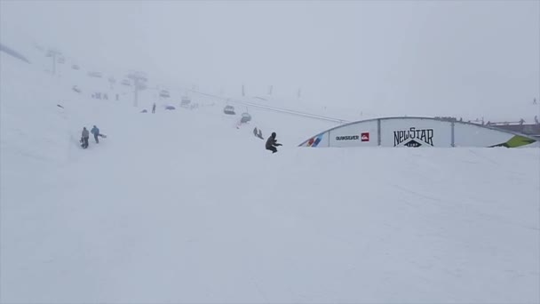 SOCHI, RUSIA - 29 DE MARZO DE 2016: Deslizamiento de snowboarder en pista curva de hierro en estación de esquí en las montañas. Deporte extremo. Nieve cae. Gente — Vídeos de Stock