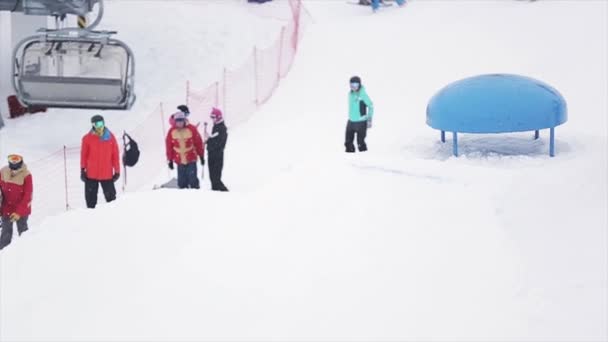 SOCHI, RUSIA - 29 DE MARZO DE 2016: Snowboarder jump, touch kicker by one foot at ski resort in mountains. Extremadamente. Esquiadores. Camarógrafo — Vídeos de Stock