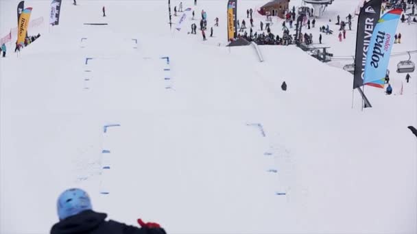 SOCHI, RUSIA - 29 DE MARZO DE 2016: Snowboarder y esquiador en salto uniforme desde trampolín, hacen volteretas extremas en el aire. Montañas nevadas . — Vídeo de stock