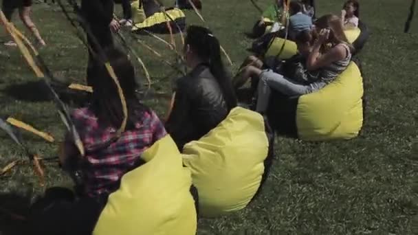 SAINT PETERSBURG, RUSSIA - JULY 16, 2015: People sit on beanbags among black and yellow waving tapes on summer festival. Sunny. Entertainment. — Stock Video