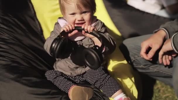 Sankt Petersburg, Ryssland-16 juli 2015: Little Bay Girl sitta på Beanbag, spela med hörlurar, man lägga den på huvudet, kastar hon det. Sommaren — Stockvideo