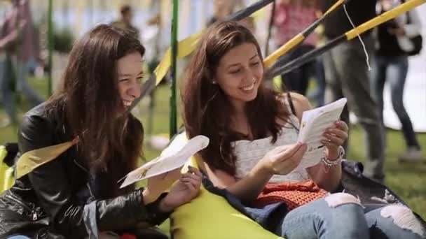 サンクトペテルブルク、ロシア - 2015年7月16日:2人の女の子が夏祭りで豆袋の上に座って小冊子を読みます。テープを振ってるエンターテイメント. — ストック動画
