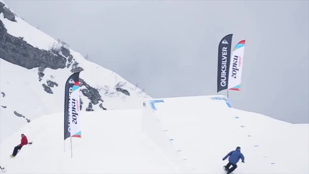 SOCHI, RUSIA - 29 DE MARZO DE 2016: Paseo de snowboarder en trampolín, se rompe abruptamente. Paisaje de montañas. Cielo gris. Concurso . — Vídeos de Stock