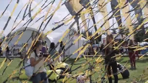 СЕНТ-ПЕТЕРБУРГ, РОССИЯ - 16 июля 2015 года: Девушка снимает друга среди размахивающих черными и желтыми лентами на летнем фестивале. Санни. Развлечения . — стоковое видео