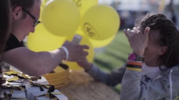 Petrohrad, Rusko-16. červenec 2015: žena s dredy ukázala telefon u stolu s krabic, žluté vzduchové balónky na letním festivalu. — Stock video