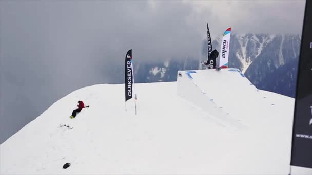 SOCHI, RUSIA - 29 DE MARZO DE 2016: Salto snowboarder desde el trampolín, hacer voltereta extrema en el aire. Paisaje de montañas. Niebla. Concurso — Vídeos de Stock